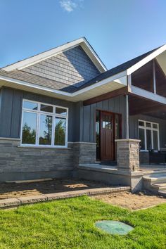 a gray house with white trim and brown doors on the front porch is surrounded by green grass