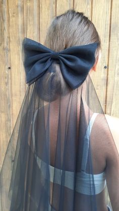 a woman wearing a veil with a black bow on it's head and her hair in a bun