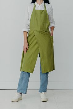 a woman standing in front of a white wall wearing green aprons and blue jeans