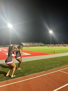 two cheerleaders standing on the sidelines at a football game with their arms around each other