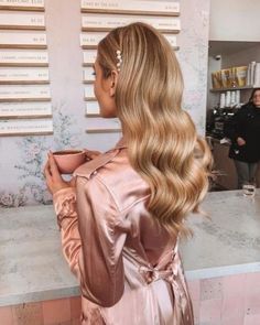 a woman with long blonde hair is holding a cup and looking at the wall behind her