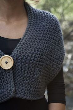 a woman wearing a gray knitted shawl with a wooden button on the front