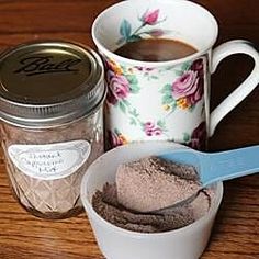 there is a cup and spoon on the table next to two jars with powder in them