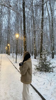 a person standing in the snow with a cell phone to their ear and looking at trees