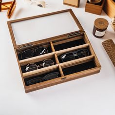 an open wooden box containing several pairs of eyeglasses and some other items on a table