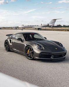 a grey sports car parked on the tarmac with an airplane in the back ground