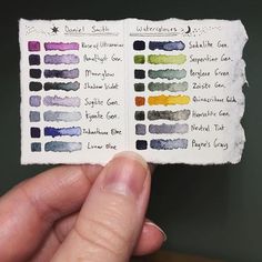 a hand holding up a small book with different colored inks on it's pages