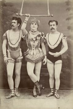 an old photo of three men in costume and one is holding a pole above his head