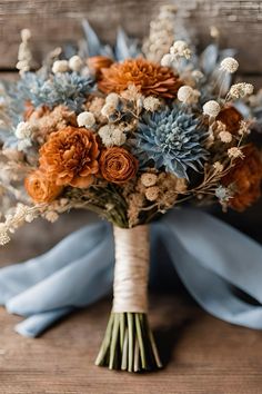 a bridal bouquet with orange and blue flowers on a wooden table, ready to be used as a wedding centerpiece