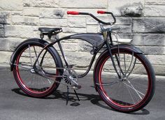 a bike with red rims parked in front of a brick wall on the street