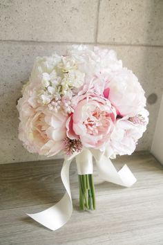 a bouquet of pink and white peonies on a table next to a wall