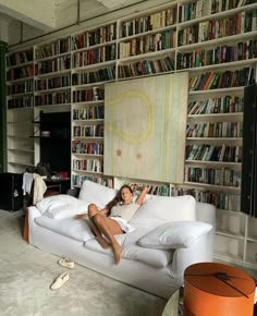 a woman laying on top of a white couch in front of a book shelf filled with books