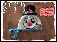 a crocheted hat with a smiling clown face on the front and side, sitting on top of a wooden floor