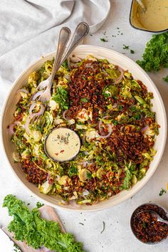 a bowl filled with salad and dressing next to other ingredients on a white tablecloth