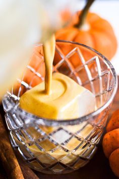 an orange juice being poured into a small glass bowl on top of a wooden cutting board