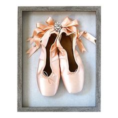 a pair of pink ballet shoes in a shadow box with a diamond brooch on top