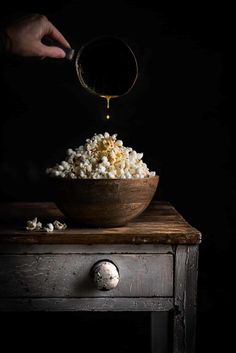 a person pouring mustard into a wooden bowl on top of a table next to an old drawer