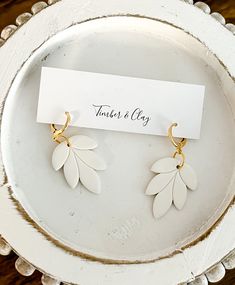 two pairs of earrings on a plate with a name card in the middle and small leaves attached to them