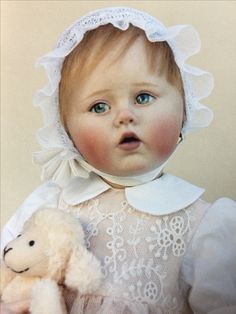 a baby doll wearing a bonnet and holding a teddy bear