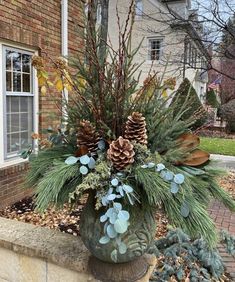 a potted plant with pine cones and greenery in front of a brick building