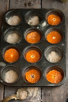 there are many oranges in the muffin tins on the wooden table with utensils