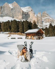 a woman laying in the snow with skis on her feet and mountains in the background