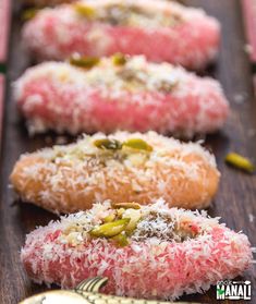 five doughnuts with different toppings on top of a wooden table next to a spoon