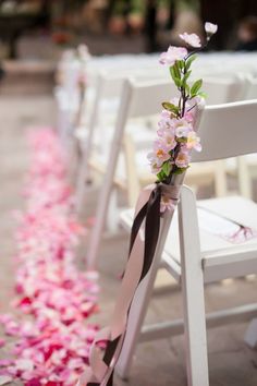 the aisle is lined with white chairs and pink flowers on them, along with ribbons