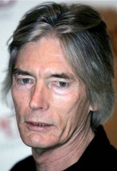 an older man with grey hair and blue eyes looks at the camera while wearing a black shirt