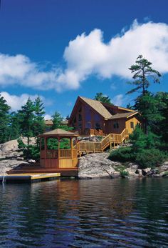 a house sitting on top of a lake next to a wooden dock in front of a forest