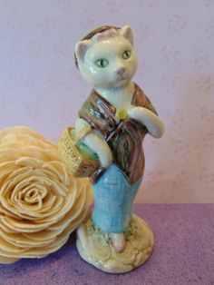 a cat figurine sitting on top of a flower next to a purple wall