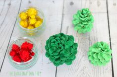 three small pine cones are sitting next to each other on a white wooden table with yellow, red and green pom - poms