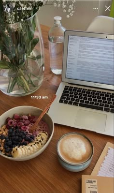 a wooden table topped with a laptop computer next to a bowl of cereal