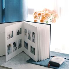 an open photo album with photos inside on a table next to a mouse and flowers