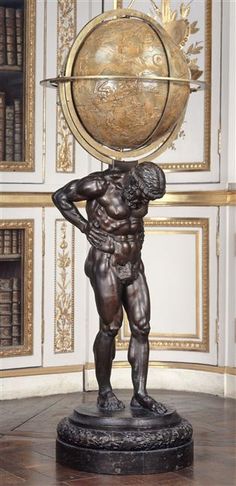 a bronze statue with a globe on it's head in front of bookshelves