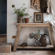 a wooden table sitting next to a wall with pictures and plants on top of it