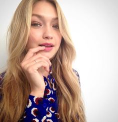 a woman with long blonde hair is posing for the camera and has her hand on her chin