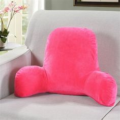 a pink pillow sitting on top of a gray couch next to a vase with flowers