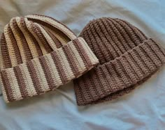 two crocheted beanies laying on top of a bed next to each other