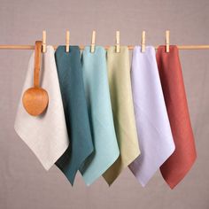 five different colored napkins hanging on a clothes line with a wooden spoon in the middle