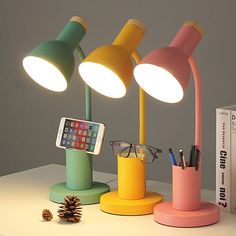 three different colored lamps sitting on top of a white table next to a book and phone