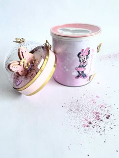 a pink tin with a minnie mouse design on it next to a canister filled with confetti sprinkles