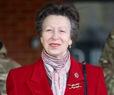 an older woman wearing a red coat and scarf with other soldiers in uniform behind her