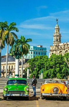 several classic cars parked in front of an old building with palm trees on the street