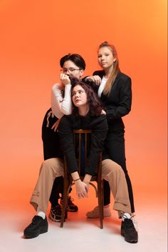 three people sitting on a chair in front of an orange background posing for the camera