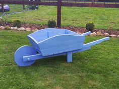 a blue wheelbarrow sitting on top of a lush green field next to a wooden fence