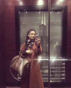 a woman taking a selfie in front of a glass elevator with her cell phone