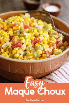 a bowl filled with corn and vegetables on top of a wooden table next to a fork