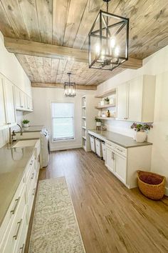 a large kitchen with white cabinets and wood flooring on the ceiling is lit by pendant lights