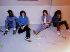 four people sitting on the floor in front of a wall with letters painted on it